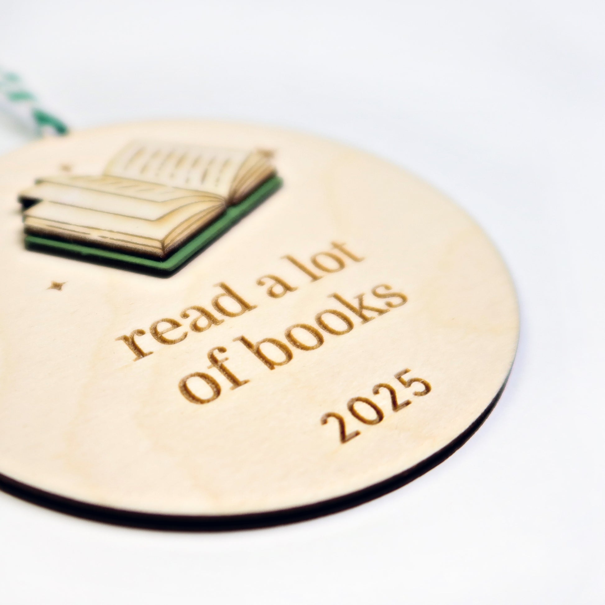Wooden ornament with book illustration and 'read a lot of books 2025' text on a white background