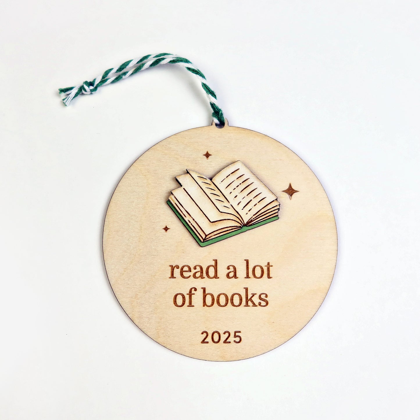 Wooden round ornament with an open book illustration and 'read a lot of books 2025' text on a white background.