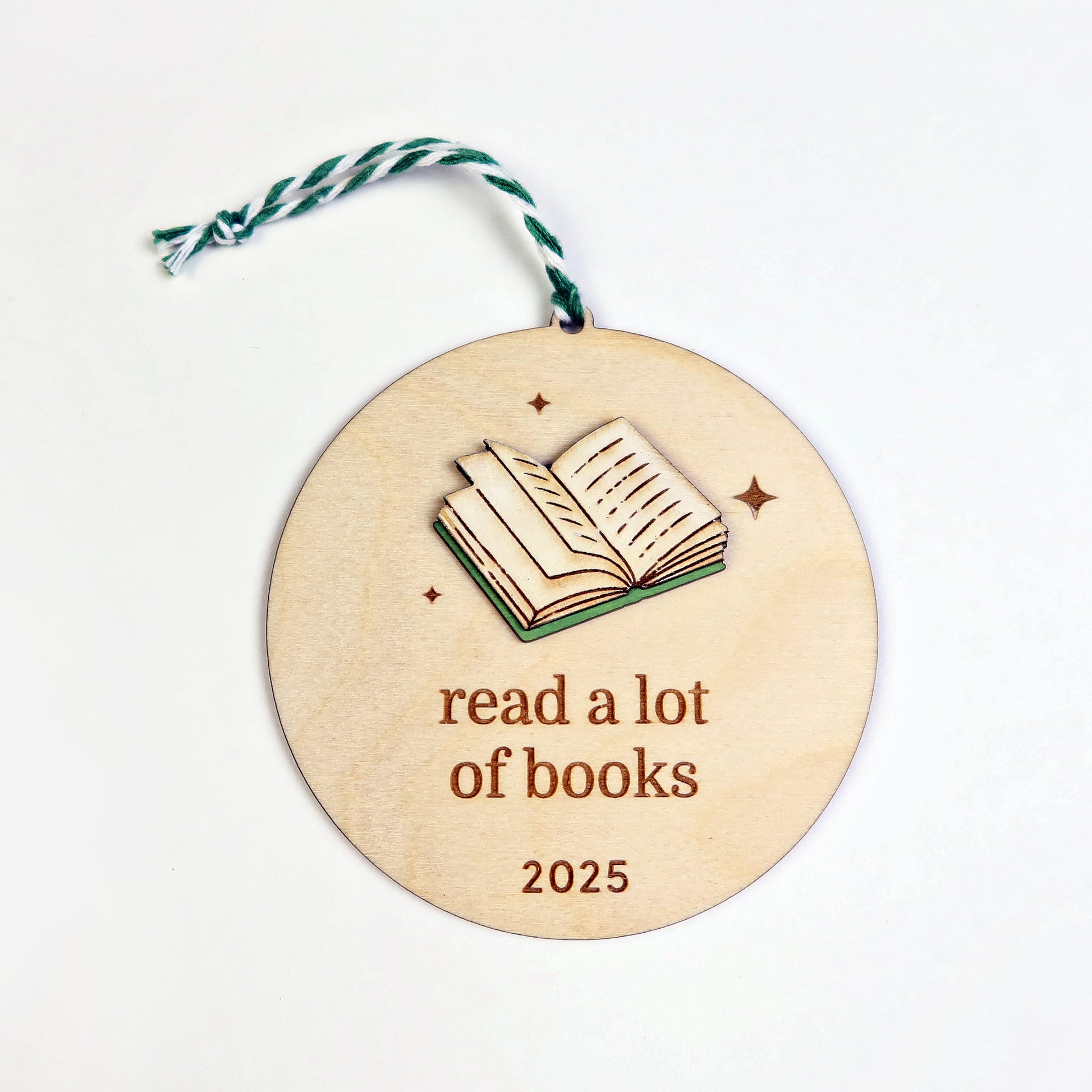 Wooden round ornament with an open book illustration and 'read a lot of books 2025' text on a white background.