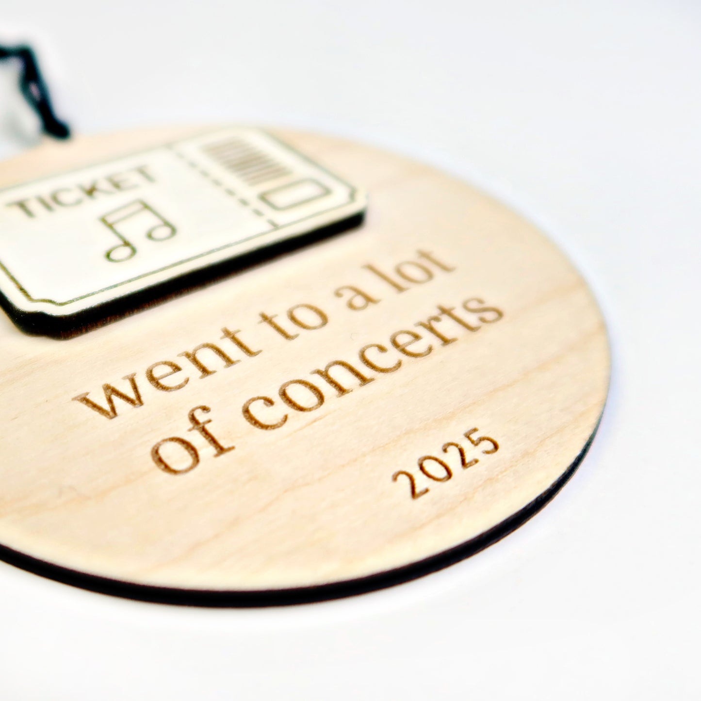 Wooden round tag with 'went to a lot of concerts' and '2025' text, featuring a ticket icon.