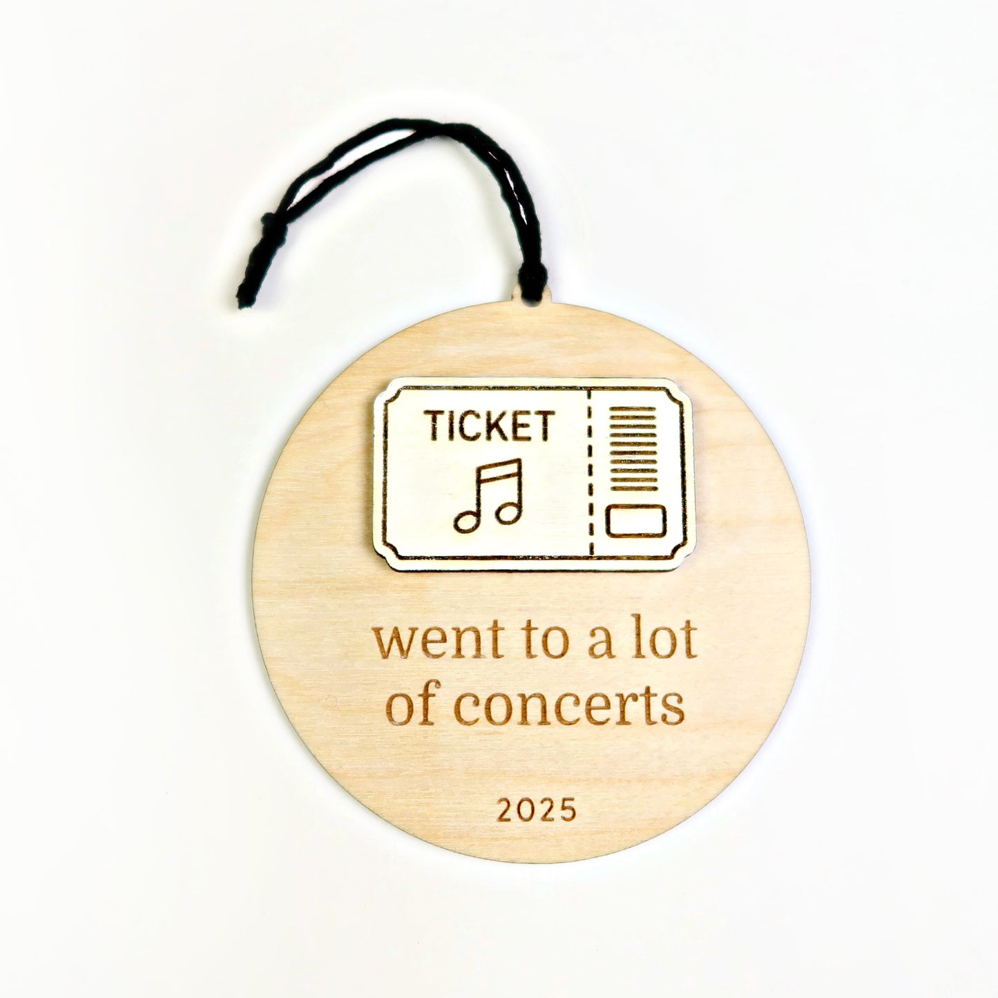 Wooden ornament with a ticket design and text 'went to a lot of concerts 2025' on a white background