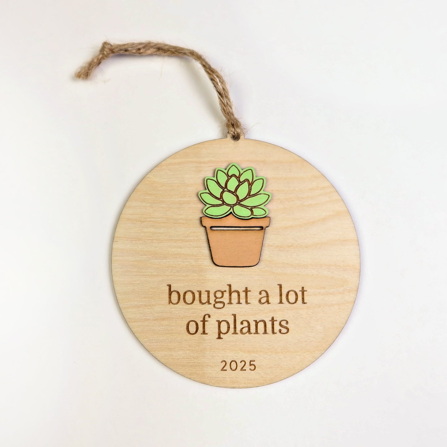Wooden ornament with a potted succulent illustration and text 'bought a lot of plants 2025' on a white background.