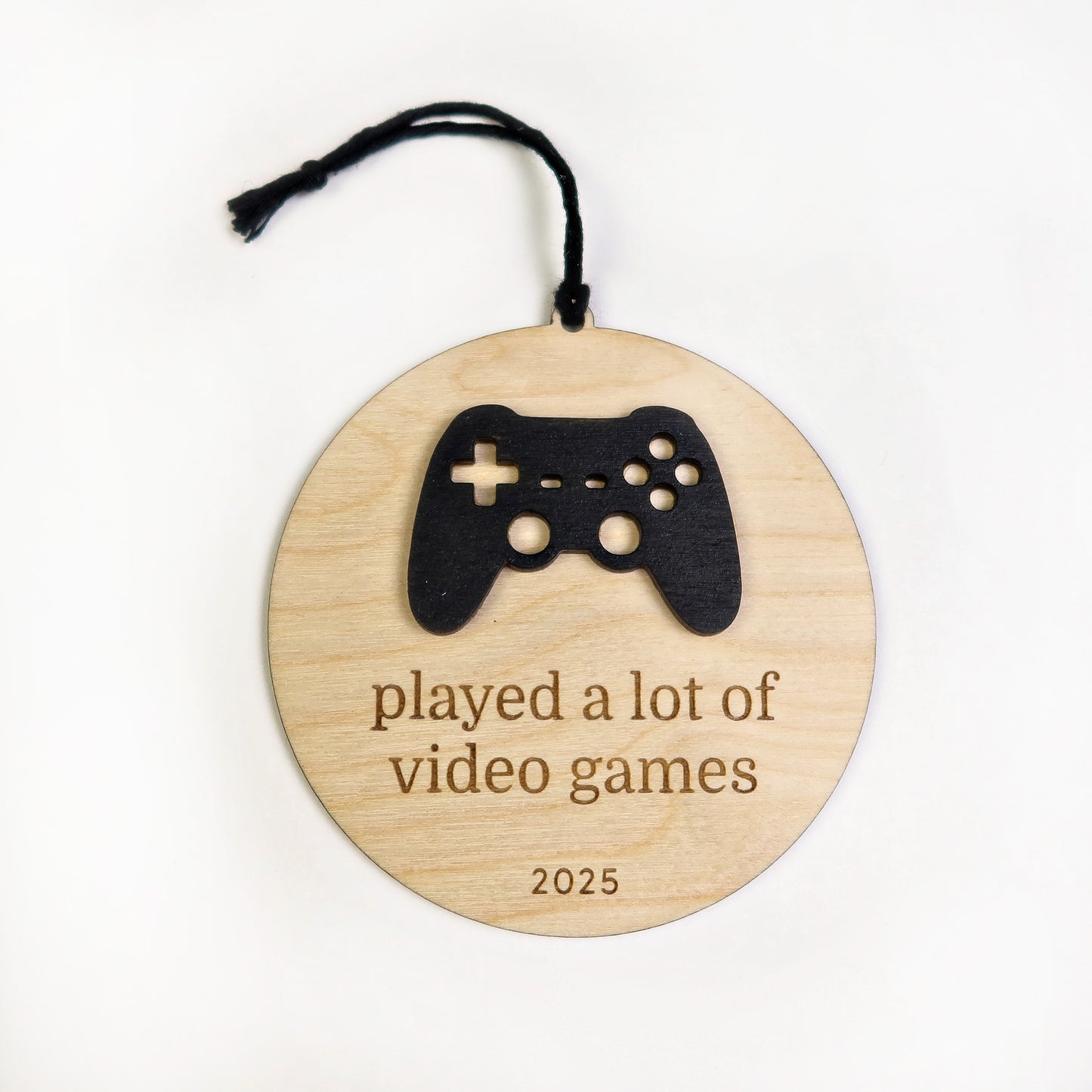 Wooden ornament with a black game controller silhouette and text 'played a lot of video games 2025' on a white background.