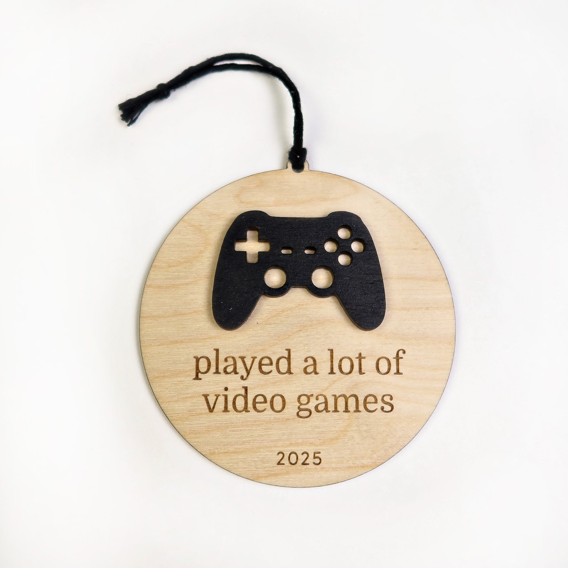 Wooden ornament with a black game controller silhouette and text 'played a lot of video games 2025' on a white background.