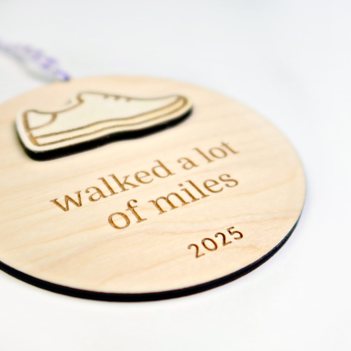 Wooden round tag with shoe icon and text 'walked a lot of miles 2025' on a white background