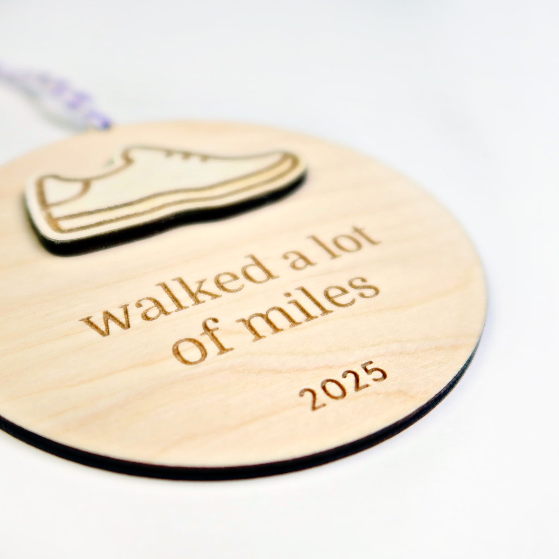 Wooden round tag with shoe icon and text 'walked a lot of miles 2025' on a white background