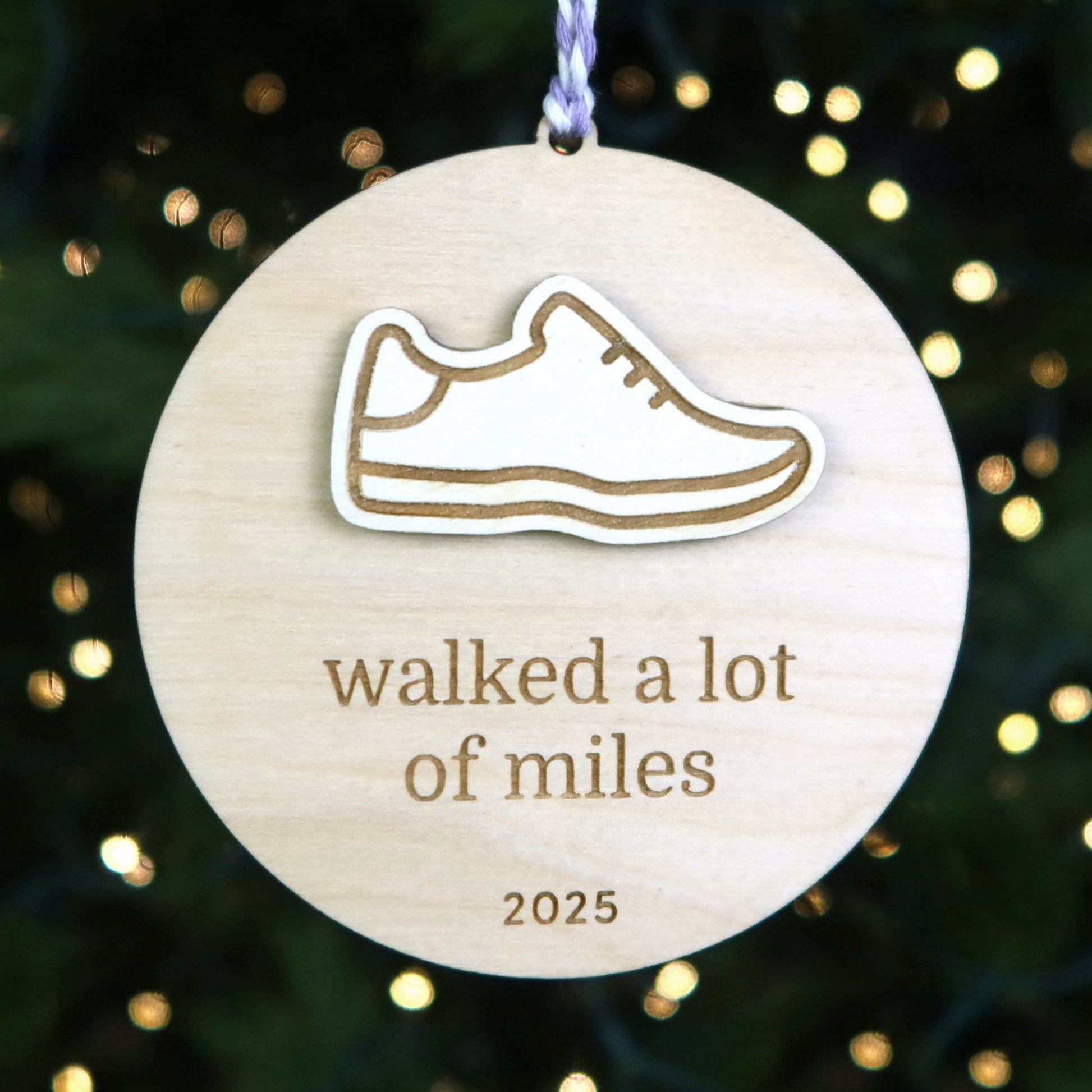 Wooden ornament with a shoe icon and text 'walked a lot of miles 2025' against a festive background.