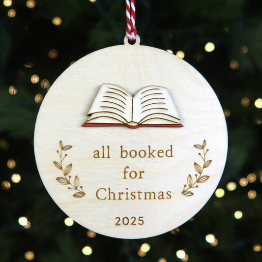 Decorative Christmas ornament with 'all booked for Christmas 2025' text and book illustration on a tree background.