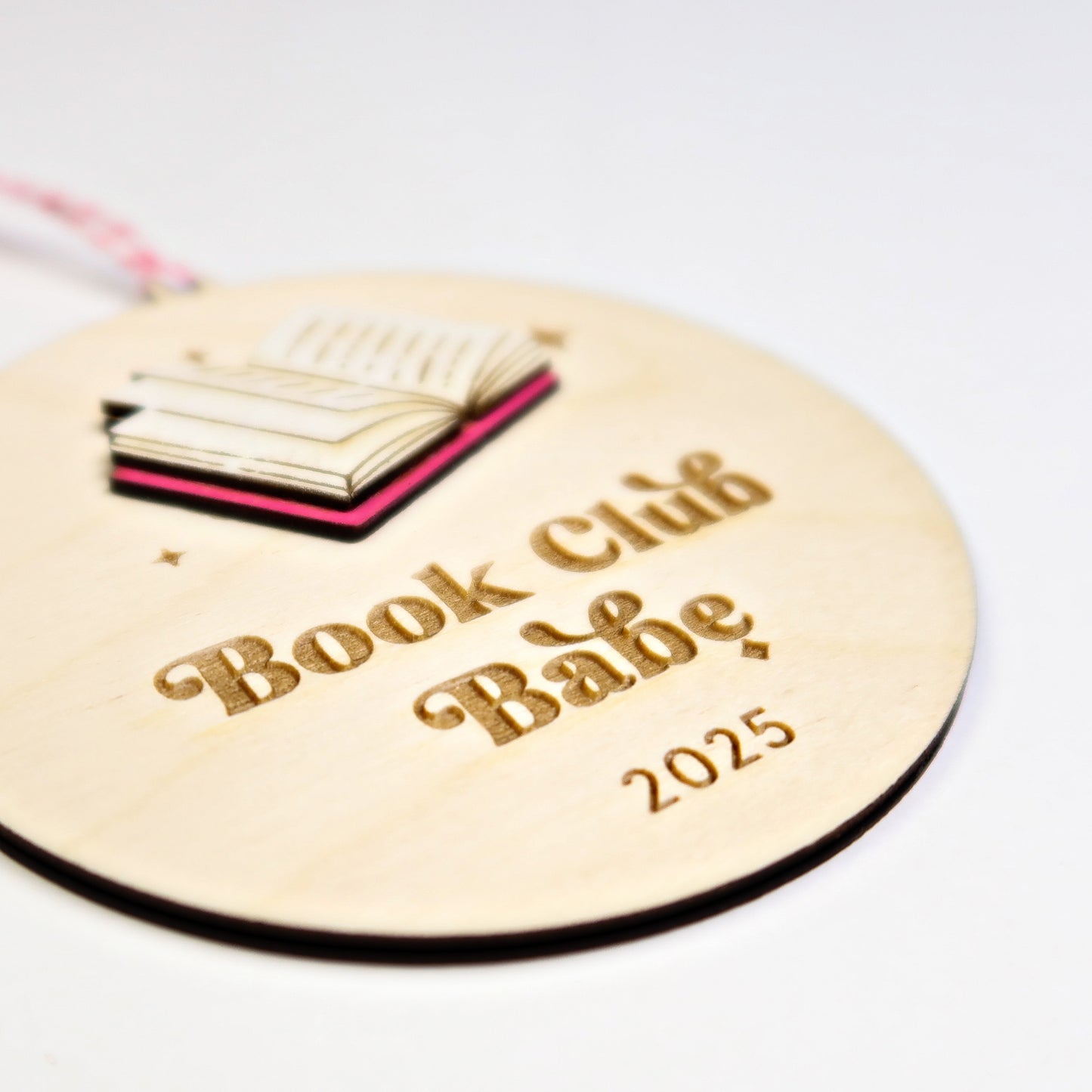 Round wooden tag with 'Book Club Babe 2025' text and book illustration on a white background