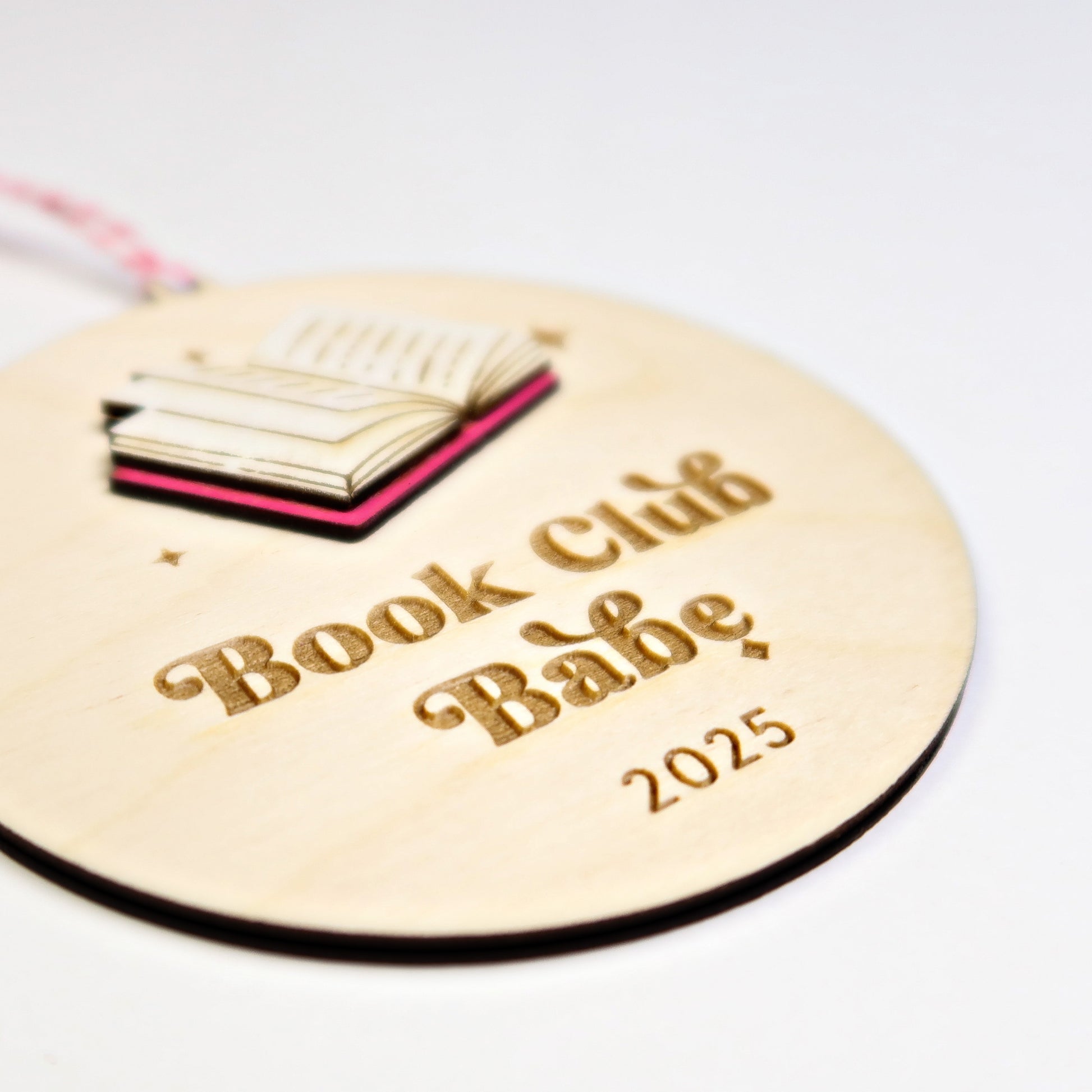 Round wooden tag with 'Book Club Babe 2025' text and book illustration on a white background