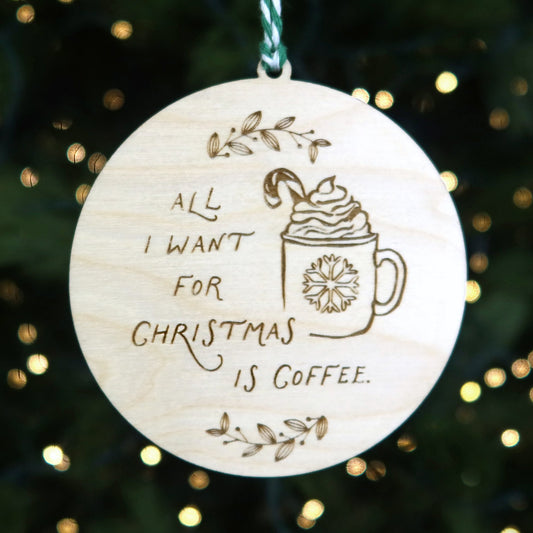 Wooden ornament with 'All I want for Christmas is coffee' text and a coffee cup illustration, hanging on a Christmas tree.