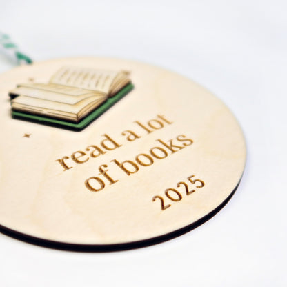 Wooden ornament with book illustration and 'read a lot of books 2025' text on a white background