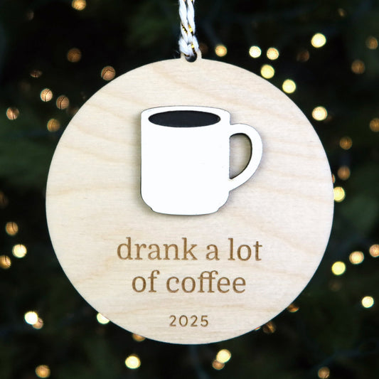 Wooden ornament with a coffee cup icon and text 'drank a lot of coffee 2025' against a festive background.