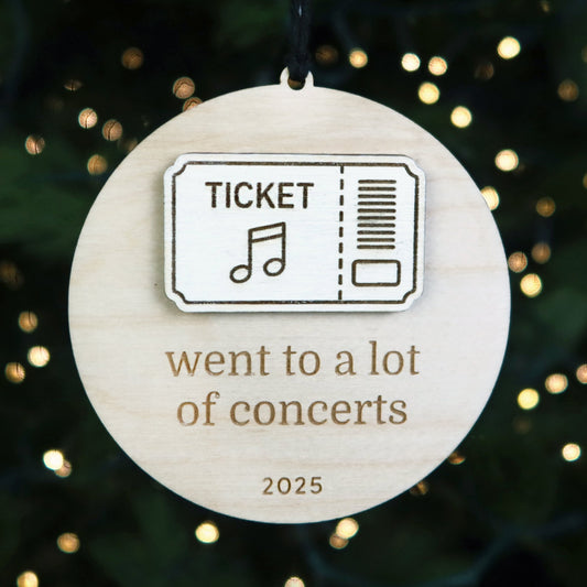 Wooden ornament with a ticket design and text 'went to a lot of concerts 2025' against a festive background.