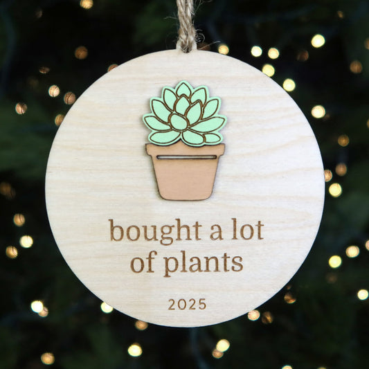 Decorative ornament with a potted plant design and text 'bought a lot of plants 2025' on a Christmas tree background.