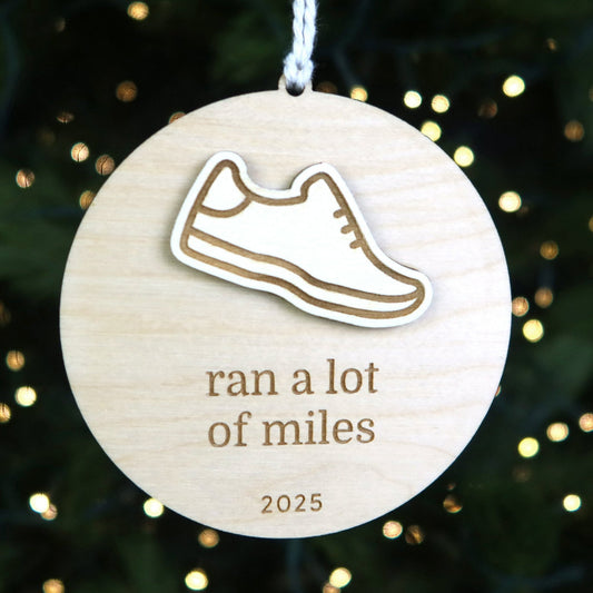 Wooden ornament with a shoe icon and text 'ran a lot of miles 2025' on a Christmas tree background.