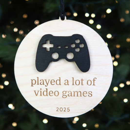Decorative ornament with a gaming controller cutout and text 'played a lot of video games 2025' on a Christmas tree.