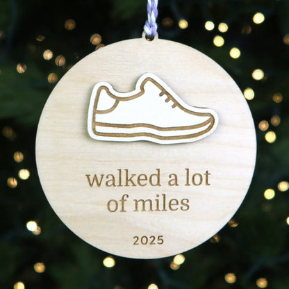 Wooden ornament with a shoe icon and text 'walked a lot of miles 2025' against a festive background.