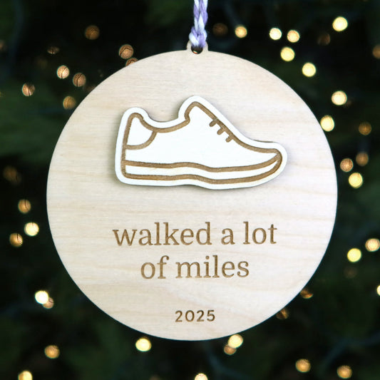 Wooden ornament with a shoe icon and text 'walked a lot of miles 2025' against a festive background.