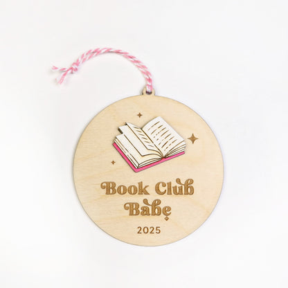 Wooden round ornament with 'Book Club Babe 2025' text and book illustration on a white background.