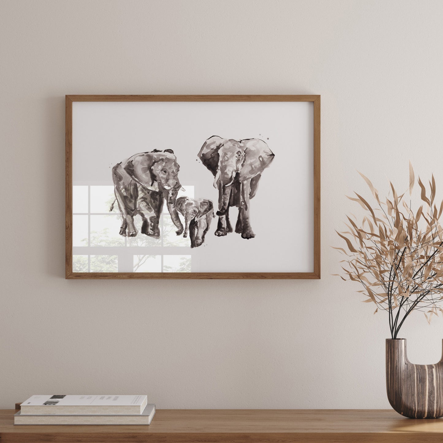 Framed artwork of elephants on a wall above a wooden shelf with books and a vase.