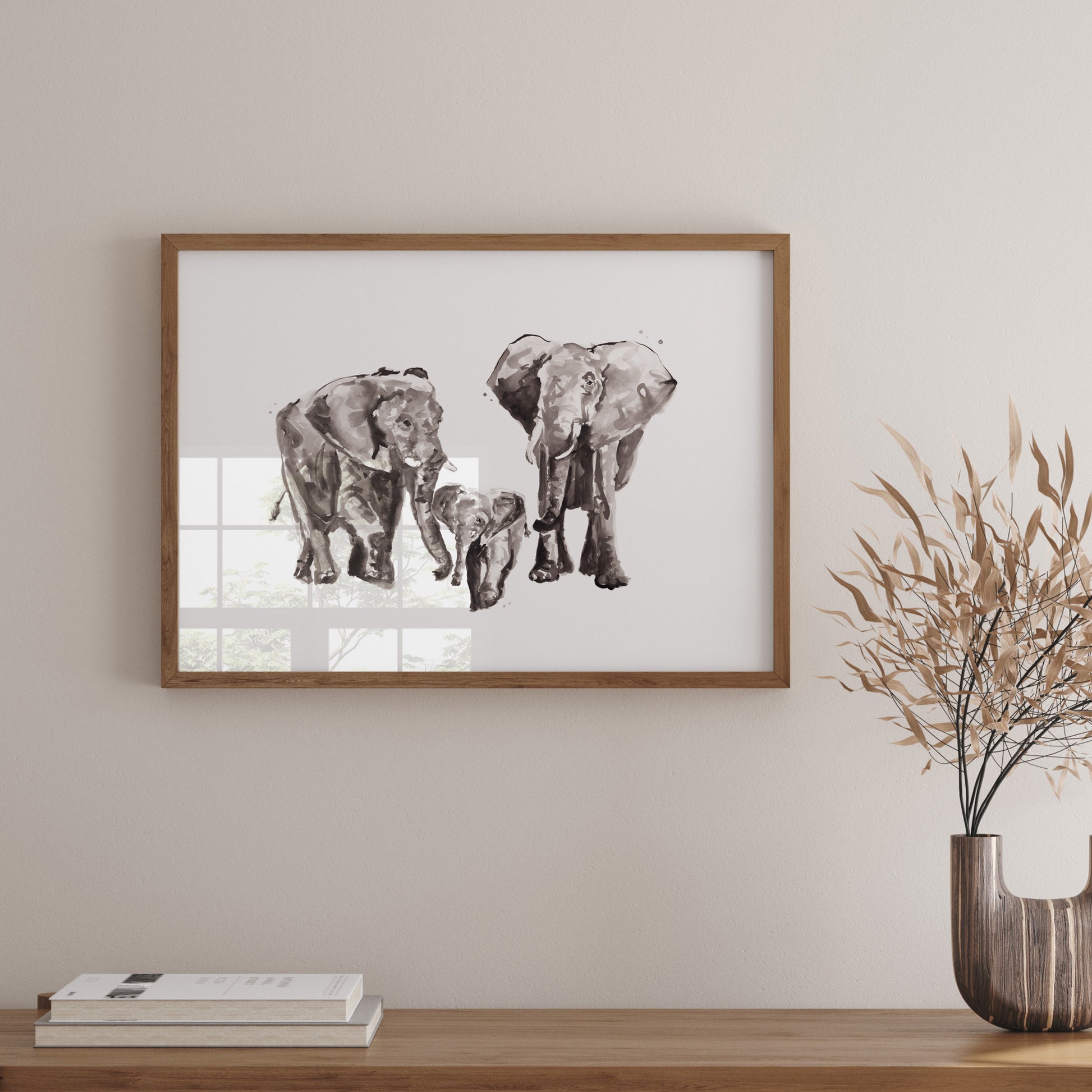 Framed artwork of elephants on a wall above a wooden shelf with books and a vase.