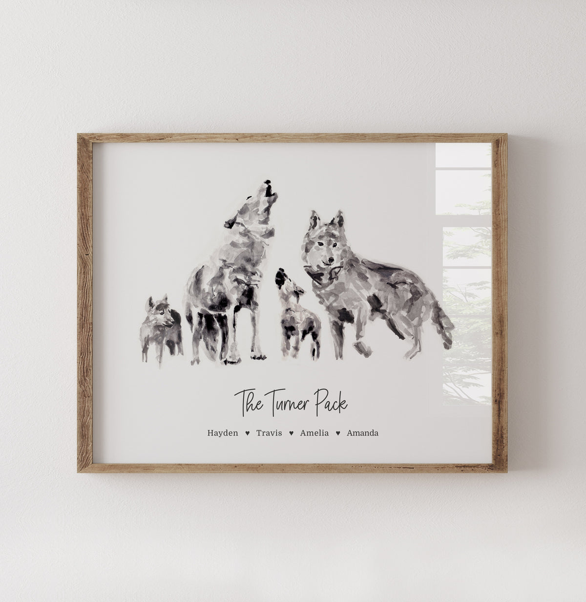A framed personalized art print featuring a watercolor-style illustration of four wolves with the text 'The Turner Pack' and names underneath, displayed on a light wall.